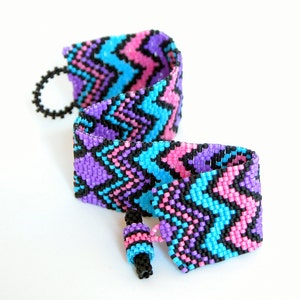May include: A beaded bracelet with a zig-zag pattern in pink, blue, and black.