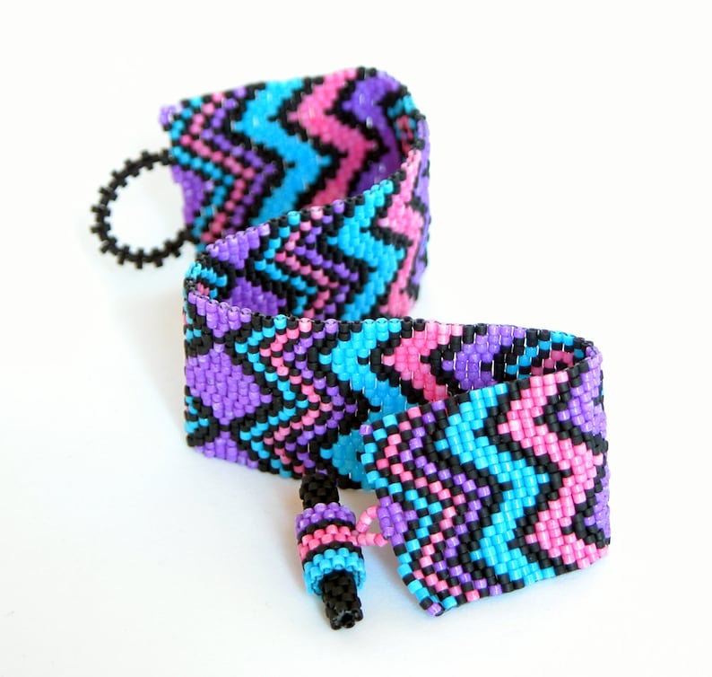 May include: A beaded bracelet with a zig-zag pattern in pink, blue, and black.