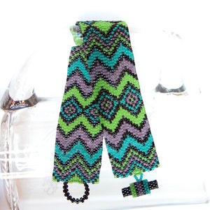 May include: Two beaded bracelets with a chevron pattern in shades of green, blue, black, and purple. The bracelets are tied together with a black cord and a small beaded charm.