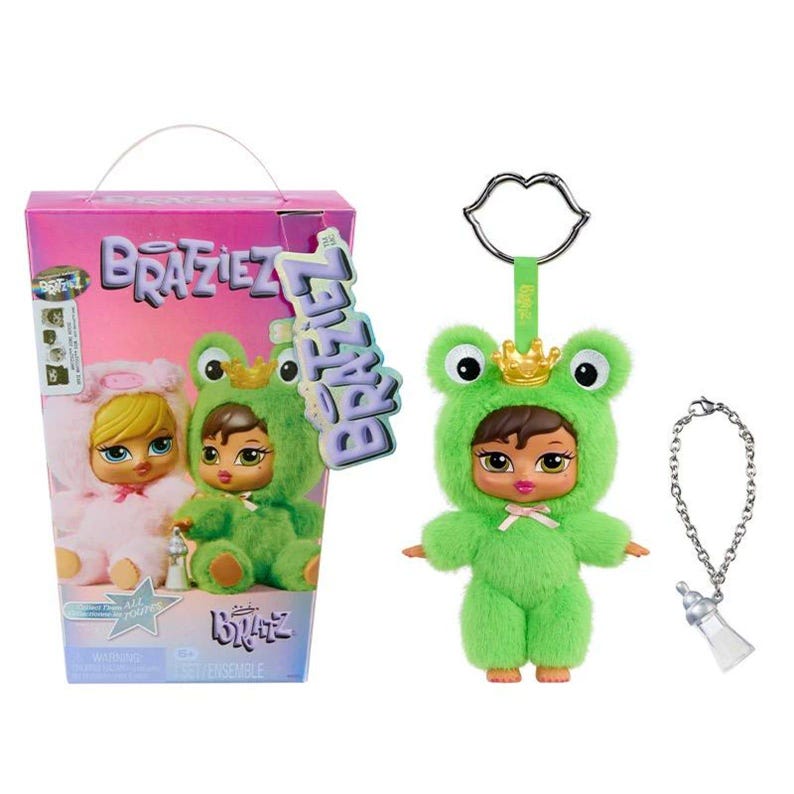 May include: A Bratz doll in a green frog costume with a gold crown, and a matching keychain with a baby bottle charm. The doll is next to a pink box with two Bratz dolls in costumes.