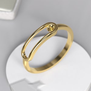 May include: A gold ring with a unique design featuring a small circle in the centre of a larger oval opening.