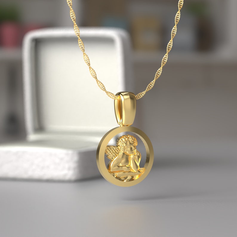Peut inclure: Un collier en cha&icirc;ne dor&eacute;e avec un pendentif rond repr&eacute;sentant une figurine de ch&eacute;rubin d&eacute;taill&eacute;e.