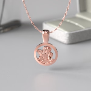 Peut inclure: Un collier en or rose avec un pendentif rond repr&eacute;sentant un ch&eacute;rubin d&eacute;taill&eacute;. Le pendentif est ajour&eacute;, laissant appara&icirc;tre les ailes et le corps du ch&eacute;rubin.