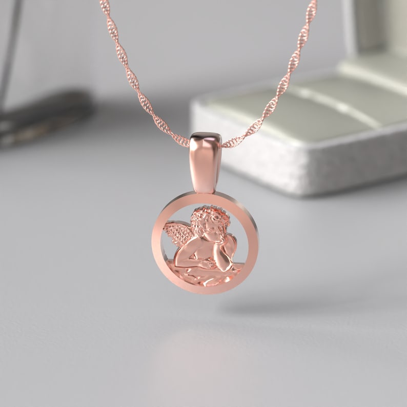 Peut inclure: Un collier en or rose avec un pendentif rond repr&eacute;sentant un ch&eacute;rubin d&eacute;taill&eacute;. Le pendentif est ajour&eacute;, laissant appara&icirc;tre les ailes et le corps du ch&eacute;rubin.