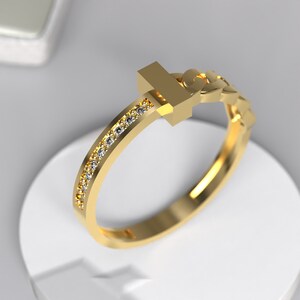 Op de afbeelding: Een gouden ring met een T-vormig ontwerp en een rij kleine diamanten rond de band.