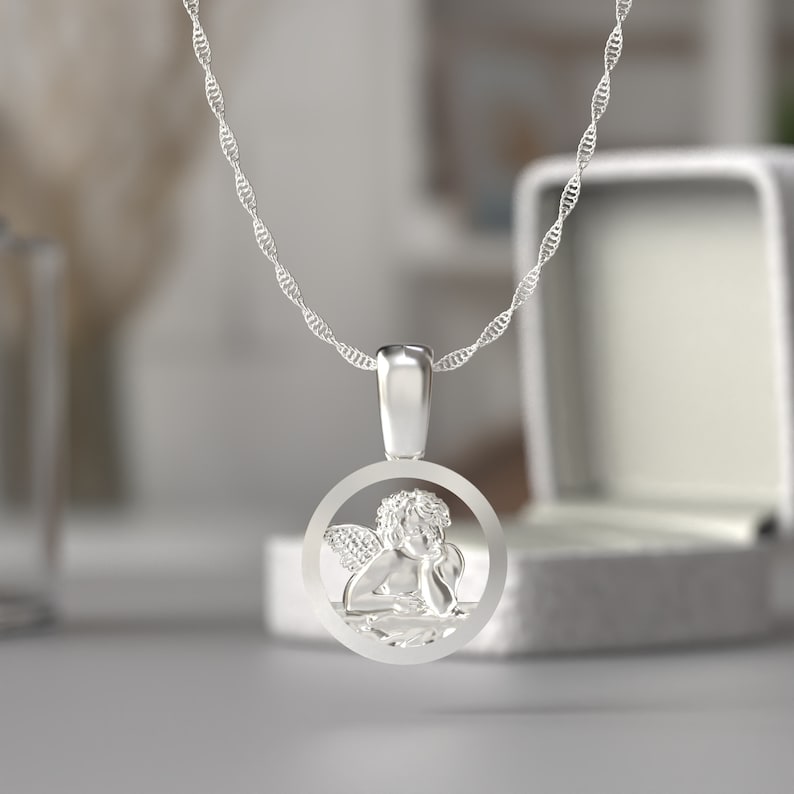 May include: A silver pendant necklace featuring a detailed angel design within a circular frame. The angel is depicted with wings and is resting its head on its hand. The necklace has a delicate, twisted chain.