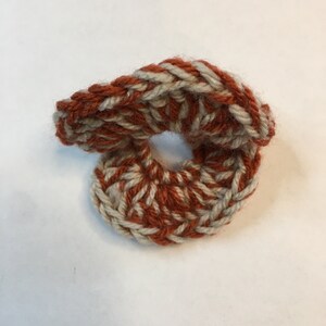 Puede incluir: Un anillo tejido a crochet hecho con hilo naranja y blanco. El anillo está retorcido y tiene un agujero en el centro.