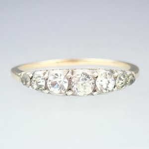 Op de afbeelding: Een gouden ring met een rij van vijf heldere ronde edelstenen.