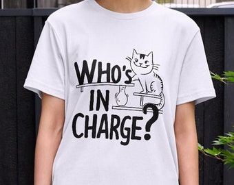 Puede incluir: Camiseta blanca con un gráfico negro de un gato sentado en un estante con el texto "Who's in charge?"