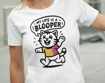 May include: White t-shirt featuring a cartoon cat wearing a yellow and pink shirt with the text "My life is a (BLOOPER)"