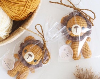 Puede incluir: Dos llaveros de crochet con forma de león, con melena marrón y cuerpo beige, empaquetados en bolsas de plástico transparentes con lazos de cuerda marrón. Cada bolsa tiene una pegatina circular blanca con un conejo marrón y el texto "Tek Yımak".