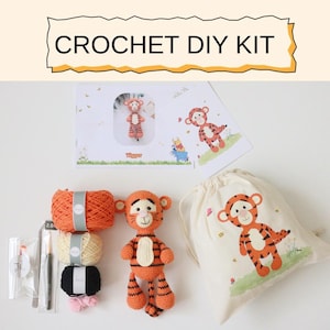 Könnte beinhalten: Ein Häkel-DIY-Kit mit Tigger-Motiv. Das Set enthält orangefarbene und cremefarbene Wolle, Häkelnadeln und ein fertiges Tigger-Plüschtier. Der Text "CROCHET DIY KIT" wird oben im Bild angezeigt.