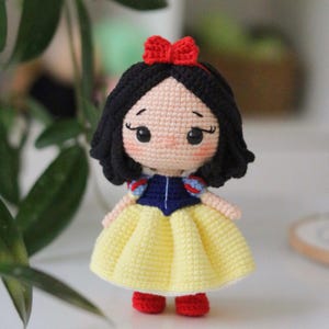 May include: A handmade crochet doll of a princess. The doll has black hair, a red bow, and a yellow dress with a blue bodice. The doll is approximately 6 inches tall.