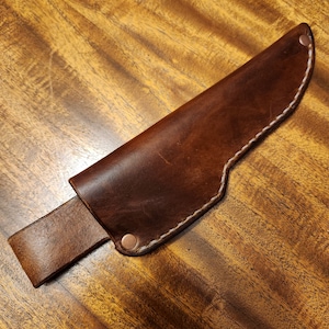 May include: A brown leather knife sheath with a white stitching detail and copper rivets.