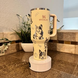 Könnte beinhalten: Eine gelbe Stanley-Reisebecher mit einem schwarz-weißen Hundedruck. Der Becher hat einen schwarzen Griff und das Stanley-Logo ist auf der Seite aufgedruckt.