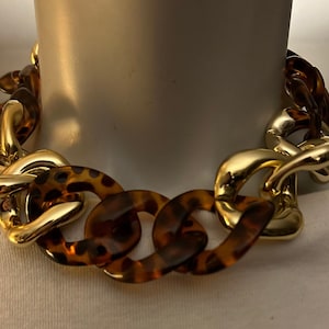 Può includere: Una collana a catena spessa dorata e marrone con un motivo a tartaruga.