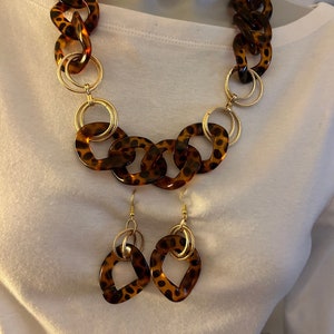 May include: A brown and gold necklace and earrings set with a large chain link design and a leopard print pattern.