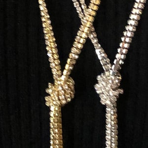Puede incluir: Dos collares largos con extremos anudados. Un collar es dorado y el otro plateado.
