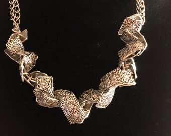 Puede incluir: Un collar de plata con una cadena y un colgante decorativo hecho de piezas cuadradas entrelazadas con diseños intrincados.