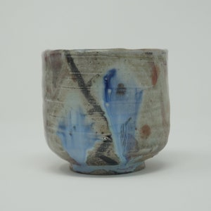 May include: A ceramic teacup with a grey glaze and blue and brown accents. The cup has a rounded shape and a wide base.