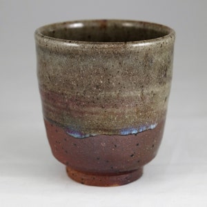 May include: A brown ceramic teacup with a speckled glaze. The cup has a wide rim and a rounded base.