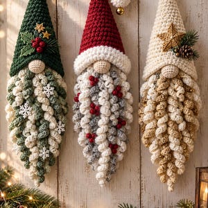 Peut inclure: Trois décorations suspendues en crochet en forme de gnome avec des chapeaux pointus. Le gnome de gauche a un chapeau vert avec du houx, celui du centre un chapeau rouge avec un pompon blanc, et celui de droite un chapeau crème avec une étoile dorée.