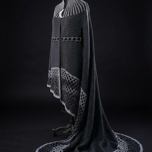 May include: A dark charcoal gray crochet cloak featuring a high collar with vertical light gray stripes, a central crescent moon accent, a horizontal braided waist detail, and a wide hem with an intricate openwork lattice pattern in light gray.