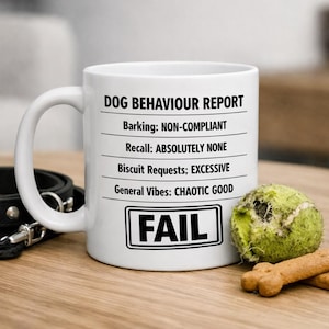 May include: White ceramic mug with a black handle, featuring a "Dog Behaviour Report" with humorous text. The report includes "FAIL" in a black box, a tennis ball, and a dog biscuit.