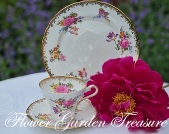 May include: A vintage teacup, saucer, and plate set with floral designs and gold trim. The set is white with pink, yellow, and purple flowers. A large, vibrant pink peony is next to the teacup. The text "Flower Garden Treasure" is at the bottom.