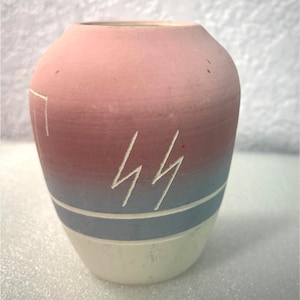 May include: A small, handcrafted vase with a gradient of colors. The top is a dusty rose, transitioning to a deep red, then to a light blue, and finally to a white base. Two lightning bolt designs are etched into the side.