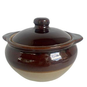 May include: A brown ceramic casserole dish with a lid. The dish has a rounded shape with a lighter beige band at the base. The lid has a small knob and the dish has handles on either side.