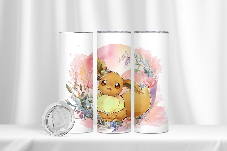 May include: A white stainless steel tumbler featuring a floral design and a cartoon image of Eevee, a Pokemon character, wearing a flower crown. The tumbler comes with a clear lid.