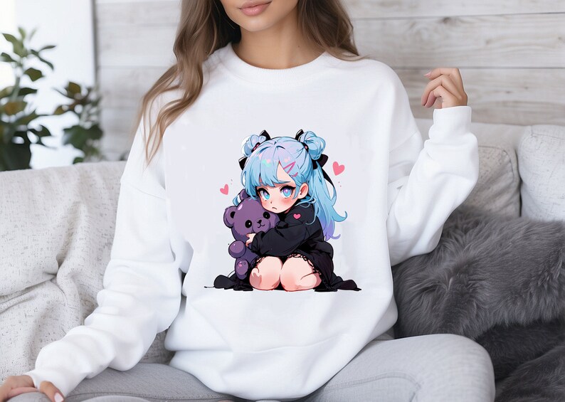Puede incluir: Sudadera blanca con un estampado gr&aacute;fico de una chica de anime de pelo azul que sostiene un oso de peluche morado. La chica tiene lazos negros en el pelo y corazones rosas alrededor.