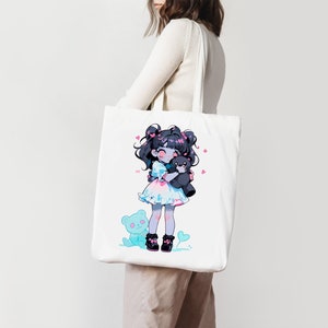 Puede incluir: Bolsa de tela blanca con una ilustraci&oacute;n colorida de una ni&ntilde;a sosteniendo un oso de peluche. La ni&ntilde;a tiene el pelo negro y lleva un vestido rosa y azul. Hay corazones rosas esparcidos alrededor de la ilustraci&oacute;n.