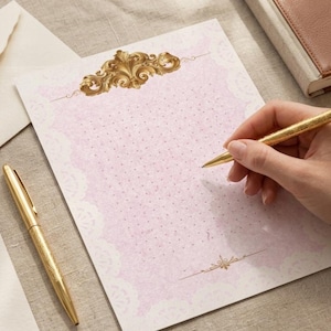 Puede incluir: Un juego de papelería rosa con un bolígrafo dorado y un bolígrafo a juego. La papelería presenta un diseño dorado decorativo en la parte superior e inferior, con un patrón de puntos. También se ve un sobre y un cuaderno.