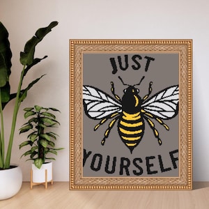 May include: Framed artwork featuring a pixelated bee with yellow and black stripes, white wings, and the words "JUST YOURSELF" in black text on a gray background. The artwork is in a gold-colored frame.