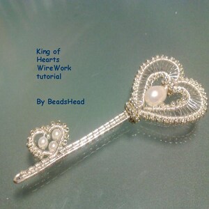 Puede incluir: Una llave de alambre plateado envuelta con una cabeza en forma de corazón y una perla en el centro. La llave está sobre una superficie azul claro. El texto "King of Hearts Wire Work tutorial By BeadsHead" está en la esquina superior izquierda de la imagen.