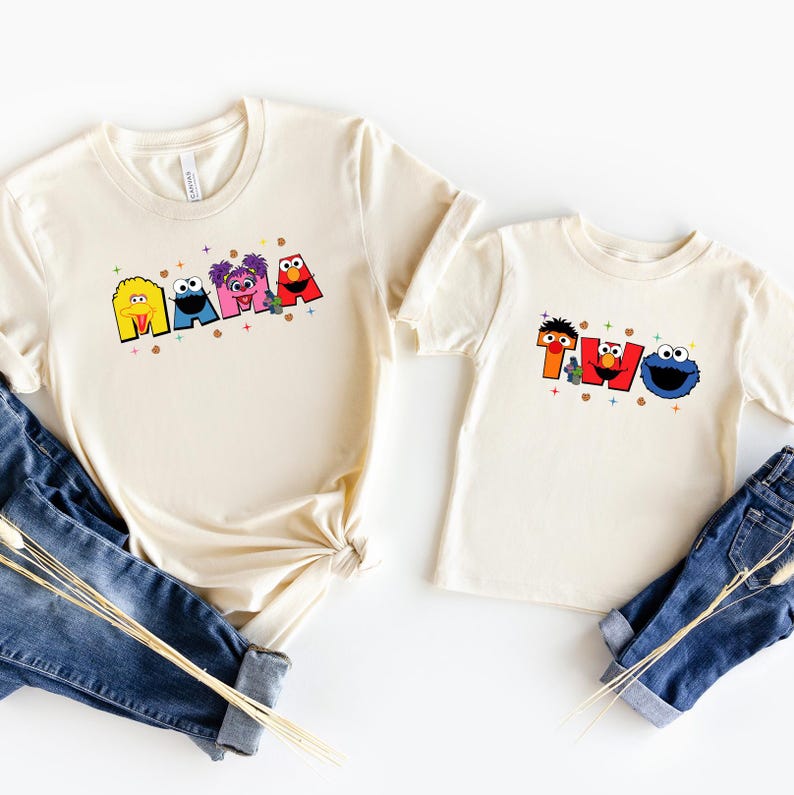 two white t-shirts with colorful cartoon character designs, including Smurfs and Cookie Monster, printed on them.