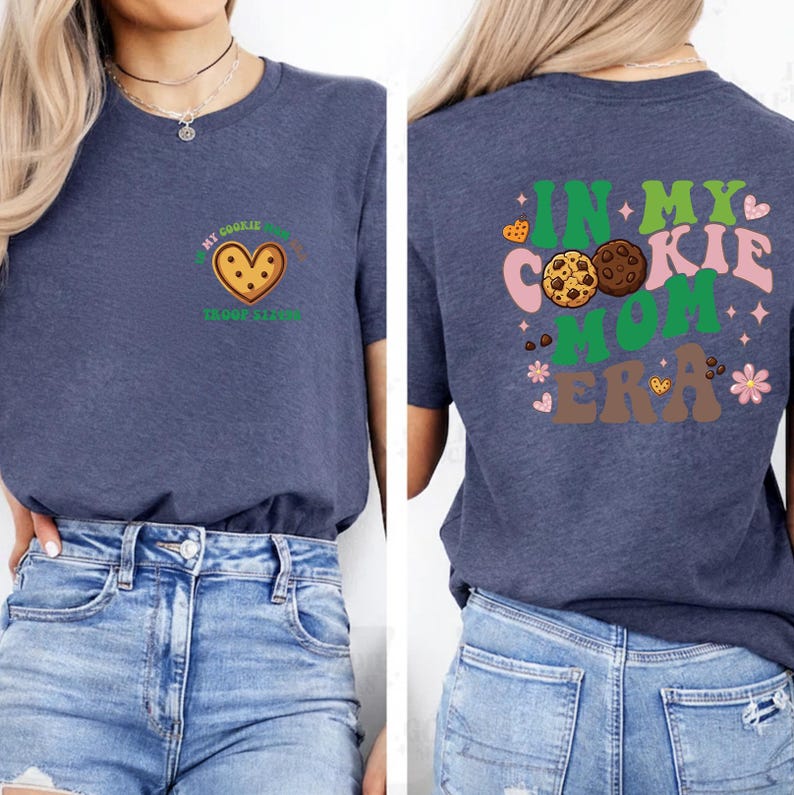 a woman wearing a blue t-shirt with a graphic design on the back. The design includes a heart and cookies, along with the text "In my cookie mom era".