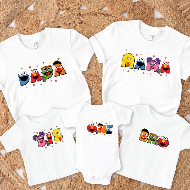 a collection of white t-shirts with colorful, cartoon-style characters printed on them. The characters include Sesame Street's iconic figures such as Big Bird, Cookie Monster, and Big Bird himself. The t-shirts are arranged in a way that showcases the variety of characters and designs, creating a visually appealing and playful display.