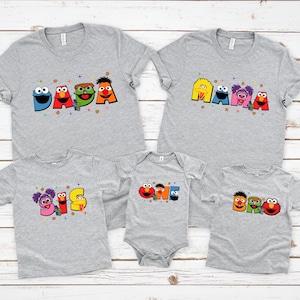 A collection of gray t-shirts with colorful cartoon character designs, including characters from the Sesame Street television series.