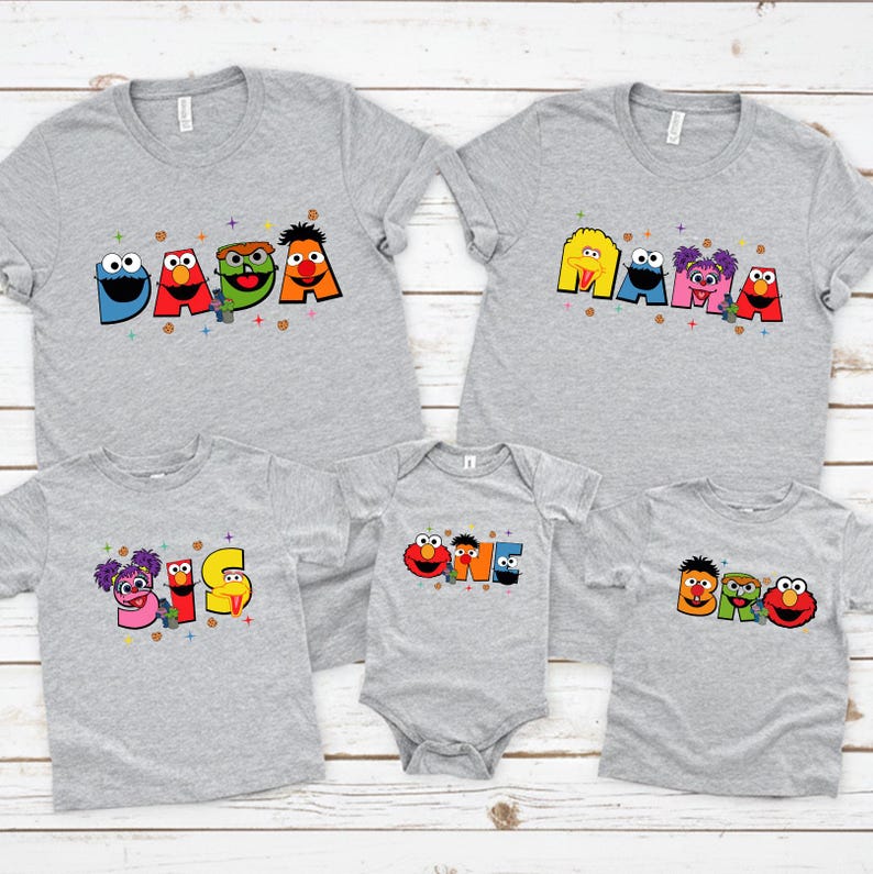 A collection of gray t-shirts with colorful cartoon character designs, including characters from the Sesame Street television series.