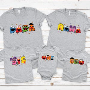 A collection of gray t-shirts with colorful cartoon character designs, including characters from the Sesame Street television series.