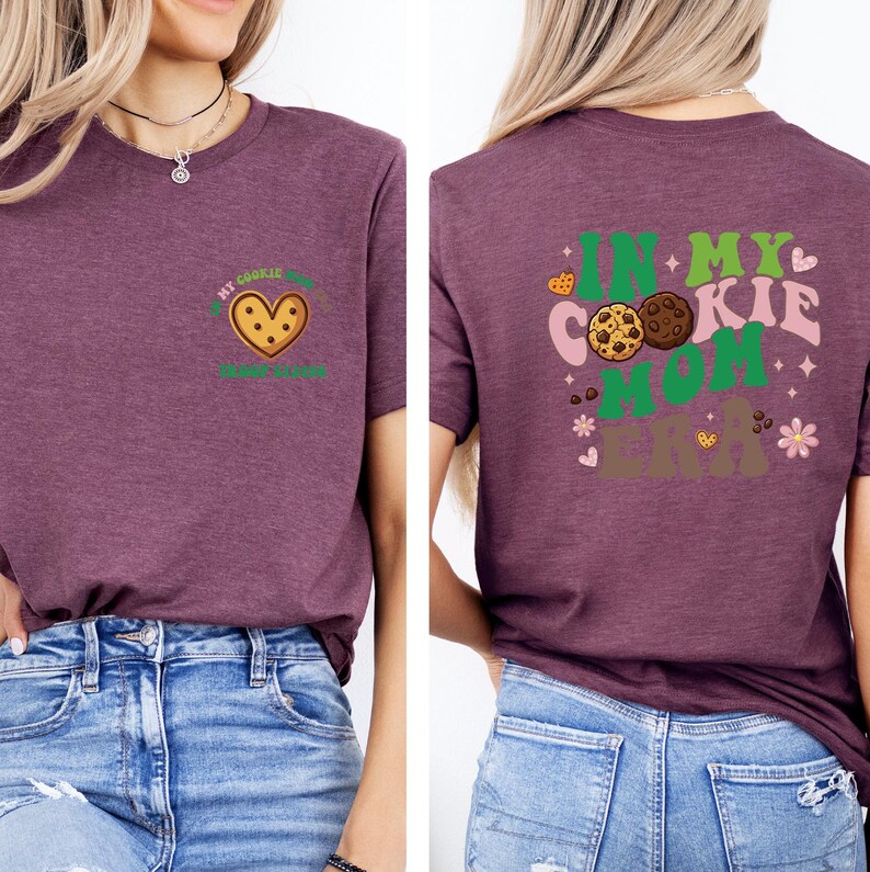 a woman wearing a purple t-shirt with a graphic design on the back. The design features a heart and cookies, along with the text "In my cookie mom era" written in a playful font.