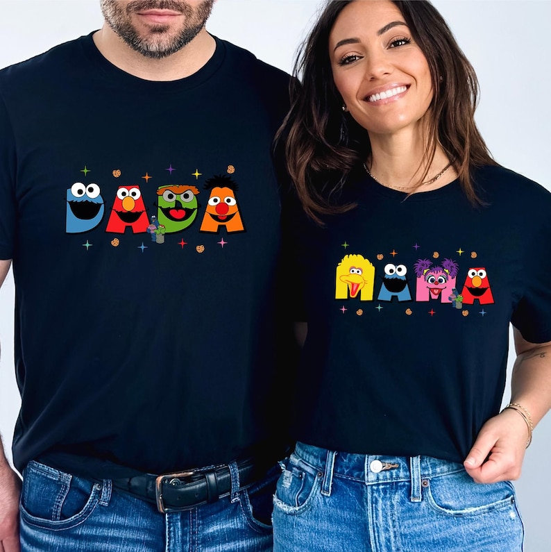 A man and a woman are standing next to each other, both wearing black t-shirts with colorful cartoon characters printed on them.