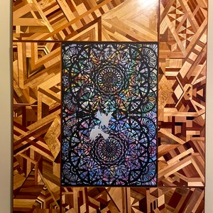 May include: A large, rectangular wall art piece made of wood with a geometric pattern. The center of the piece features a black and white mandala design with a colorful background.