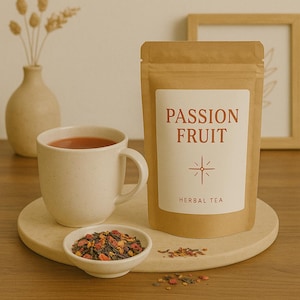May include: A beige ceramic mug filled with red liquid sits on a round, light-colored tray, next to a small white bowl of tea leaves. A brown paper bag labeled "PASSION FRUIT HERBAL TEA" is also on the tray. A vase and a framed picture are in the background.