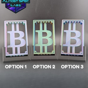 May include: Three Bitcoin-themed display pieces in a row, each with a different color scheme. The Bitcoin symbol is prominently featured within a rectangular frame. The text "OPTION 1", "OPTION 2", and "OPTION 3" are below each piece. The Almost-Spec Labs logo is in the upper left corner.