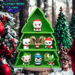 Könnte beinhalten: Eine grüne, weihnachtsbaumförmige Vitrine mit Miniaturfiguren von Weihnachtscharakteren. Zu den Figuren gehören der Weihnachtsmann, ein Schneemann, ein Rentier, ein Bär, ein Elf, ein Pinguin und ein grüner Teufel. Das Almost-Spec Labs Logo ist sichtbar.