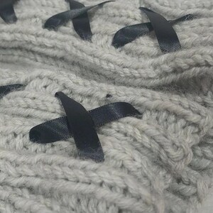May include: Gray knitted fabric with black ribbon crisscrossing the fabric. The fabric is soft and textured.